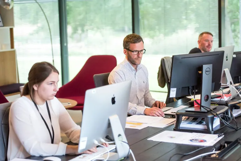 Suivi après un salon, relancer et convertir vos leads Équipe au bureau devant des écrans et des documents imprimés, au moment du suivi après un salon