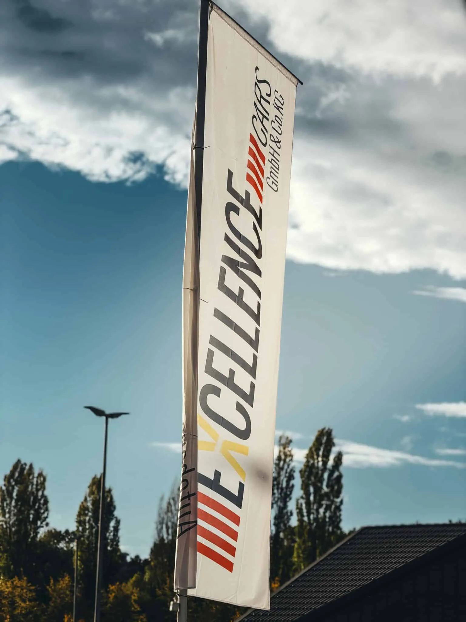Oriflamme publicitaire verticale sur mât flottant au vent devant un ciel nuageux