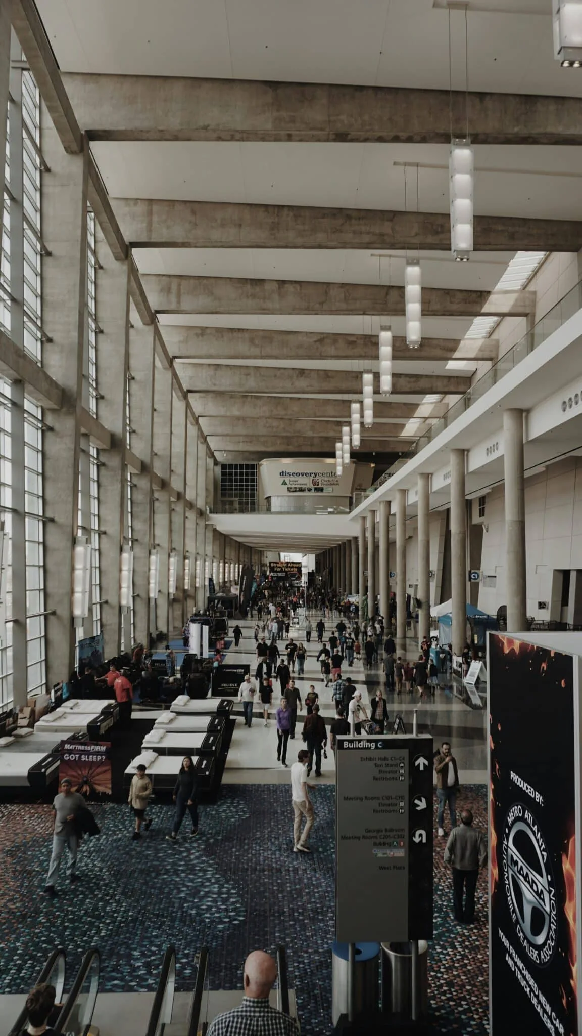 Grand hall d'un centre de congrès avec colonnes, visiteurs et signalisation vers les salles d'exposition