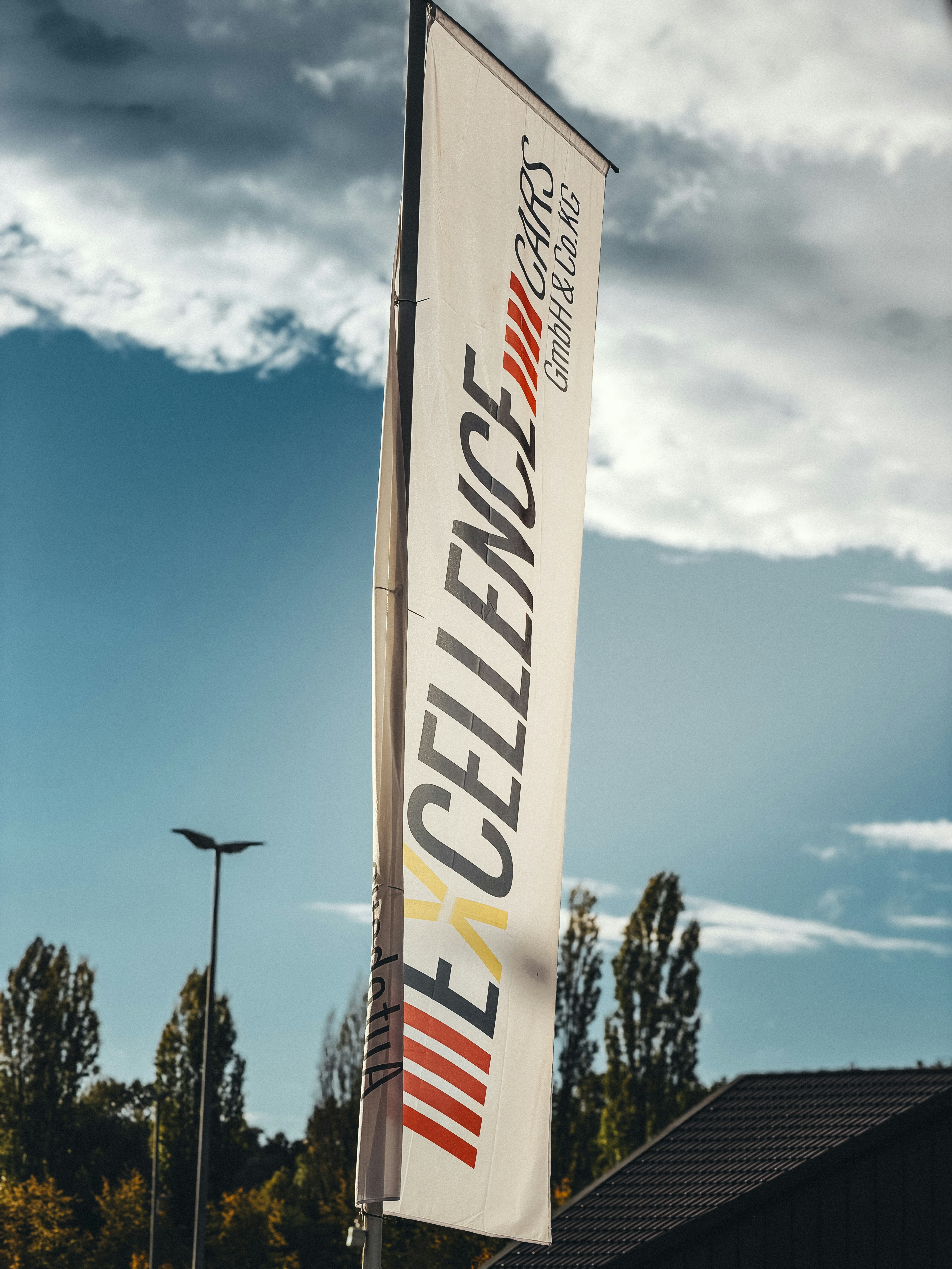 Oriflamme publicitaire verticale sur mât flottant au vent devant un ciel nuageux